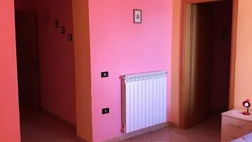A room with pink walls, a white radiator, a bed, and a door leading to another room.