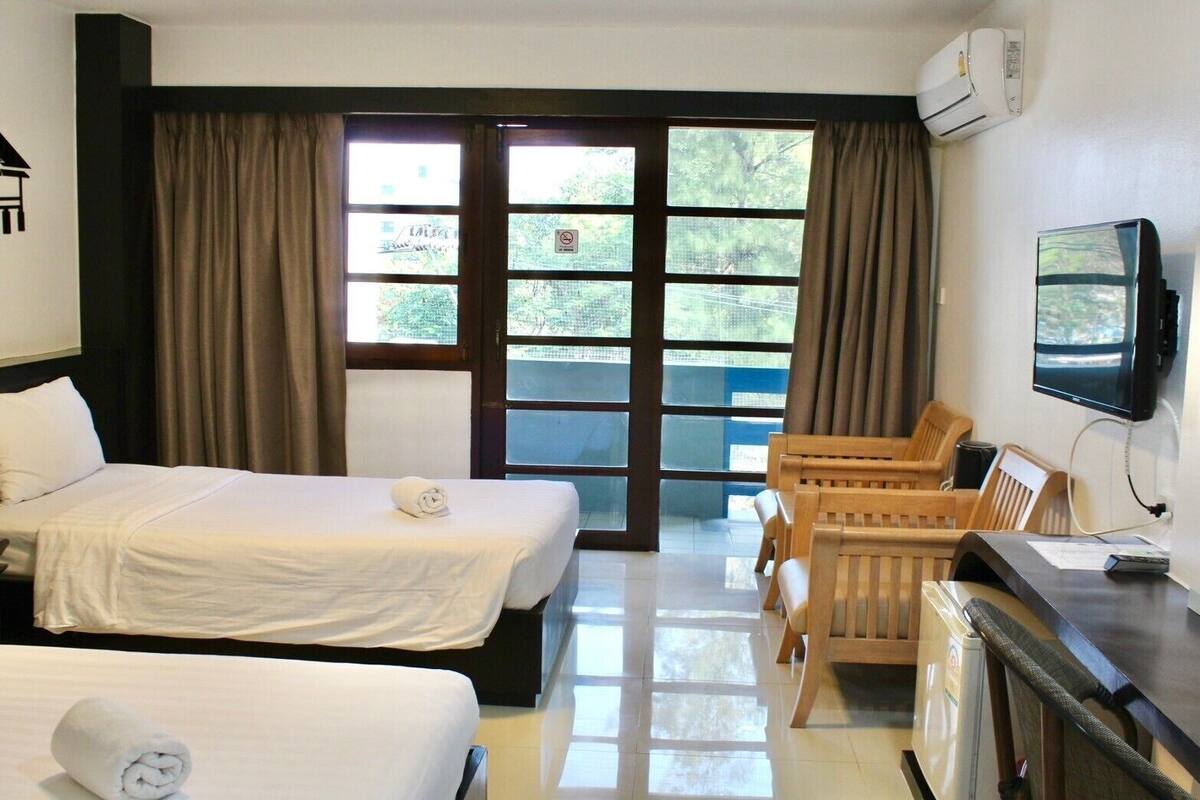 A hotel room with two beds, a desk with a chair, a television, and large windows with curtains.