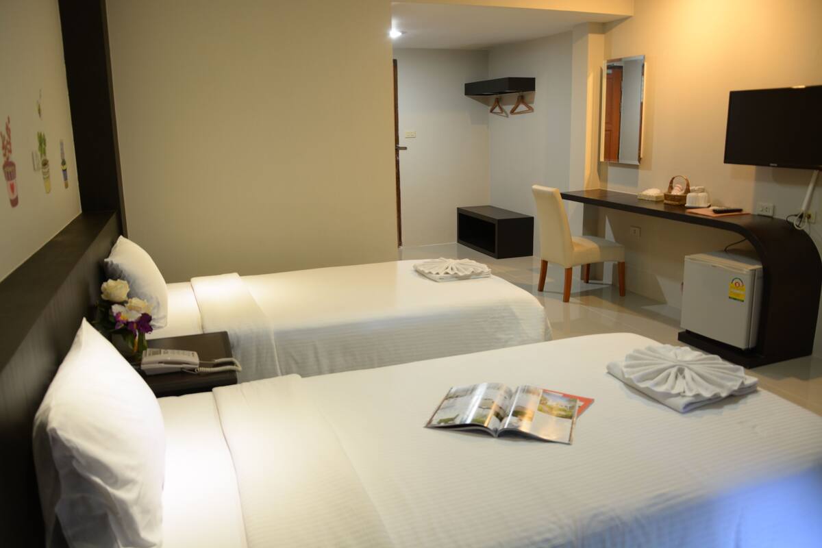 A hotel room with two beds, a desk, a chair, a television, and a refrigerator.