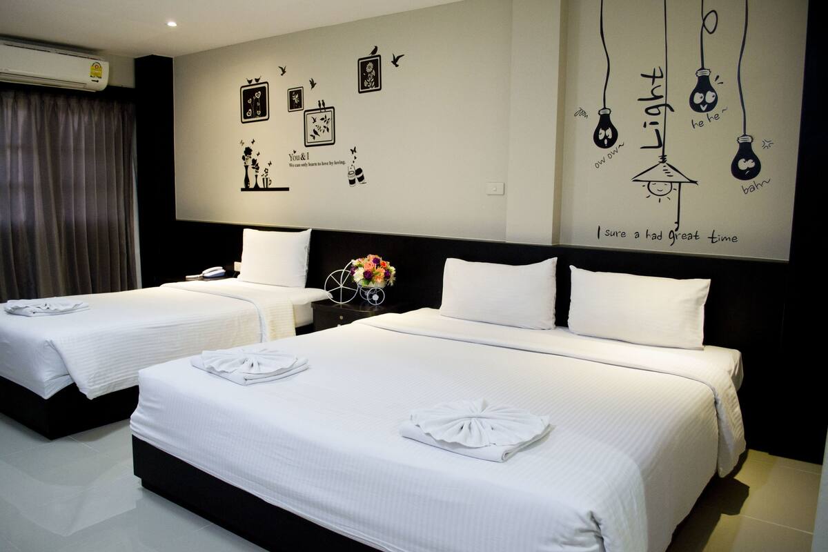 A hotel room with two beds, white linens, a wall with decorative light bulb drawings, and a window with curtains.