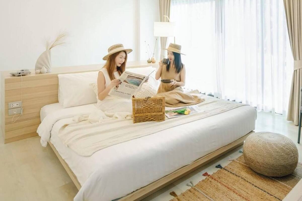 A bed with white bedding, a bedside table with a lamp, and a window with curtains.