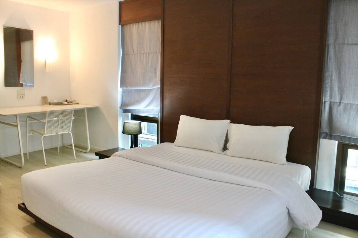 A hotel room with a large bed, a desk, a chair, a lamp, and a window with curtains.