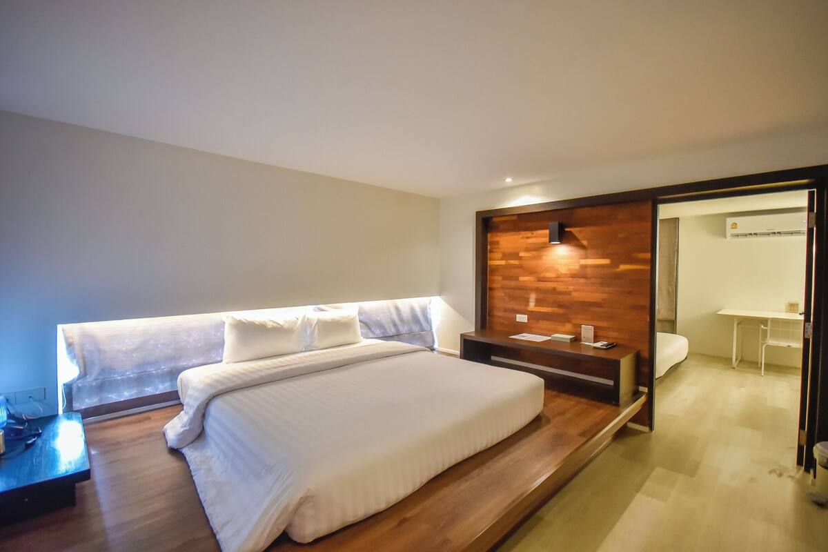 A modern hotel room with a wooden bed, a desk, and a small seating area.