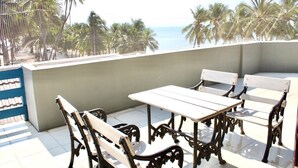 Un balcon avec une table et des chaises, d’où l’on peut admirer des palmiers et une plage.