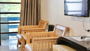 Une chambre d’hôtel avec deux chaises en bois, une petite table, un téléviseur fixé au mur et une fenêtre avec des rideaux.
