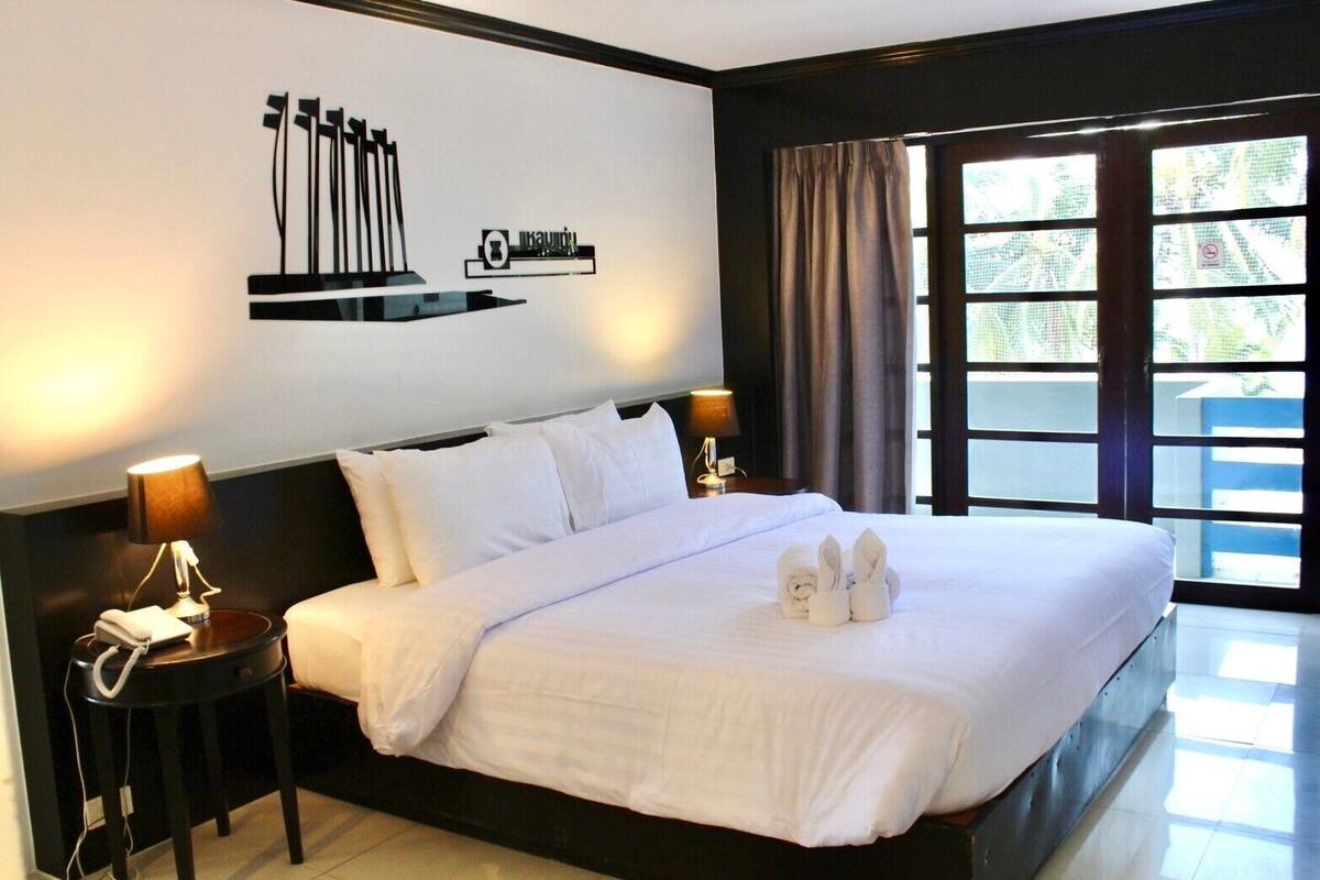 A hotel room with a large bed, two bedside tables with lamps, a wall-mounted artwork, and a view through a window with curtains.