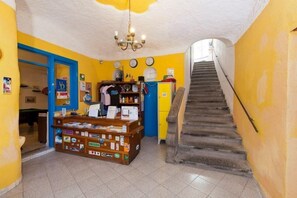 Eine Treppe führt zu einer zweiten Etage, ein Empfangsschalter mit diversen Gegenständen und eine Uhr an der Wand.