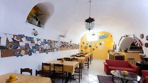 A cozy dining area with a long table and chairs, a red sofa, and a small coffee table. - Ring Hostel (Forio)