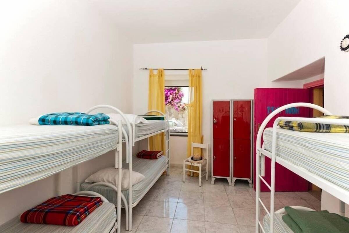 Ein Schlafsaalzimmer mit Etagenbetten, einem kleinen Schreibtisch, einem Stuhl, einem Kleiderschrank und einem Fenster mit Vorhängen.
