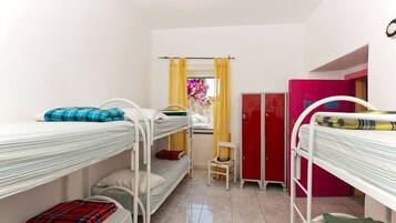 Een studentenkamer met stapelbedden, een klein bureau, een stoel, een kledingkast en een raam met gordijnen.
