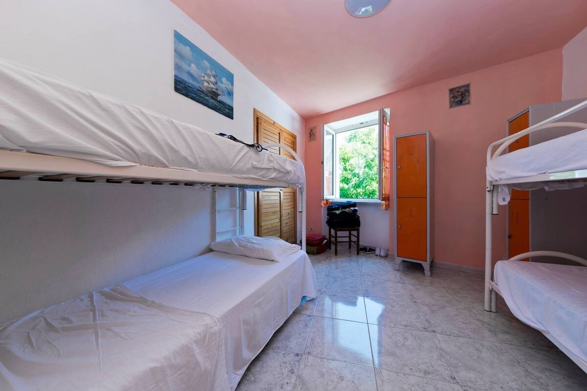 Ein Schlafsaalzimmer mit Etagenbetten, einem kleinen Schreibtisch und einem Fenster mit Blick auf Grünflächen.