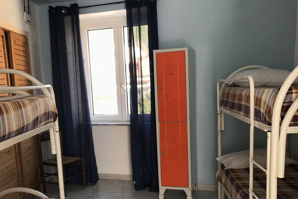 Ein Schlafraum mit Etagenbetten, einem Fenster mit Vorhängen, einem Kleiderschrank und einem Fliesenboden.