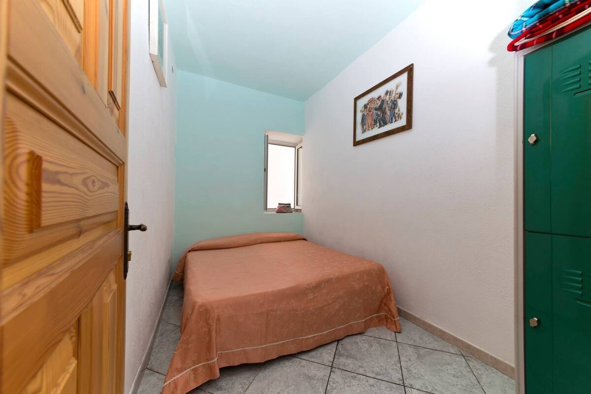 Ein Schlafzimmer mit einem Bett, einem Holzschrank, einer grünen Tür und einem kleinen Fenster.
