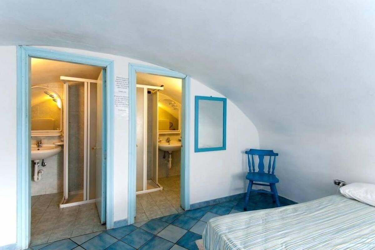 Ein kleines Schlafzimmer mit Bett, Stuhl und einem Badezimmer mit Waschbecken und Spiegel.