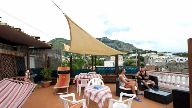 A terrace with outdoor seating, a hammock, and a view of the town and mountains. - Ring Hostel (Forio)