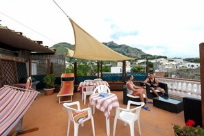 A terrace with outdoor seating, a hammock, and a view of the town and mountains. - Ring Hostel (Forio)