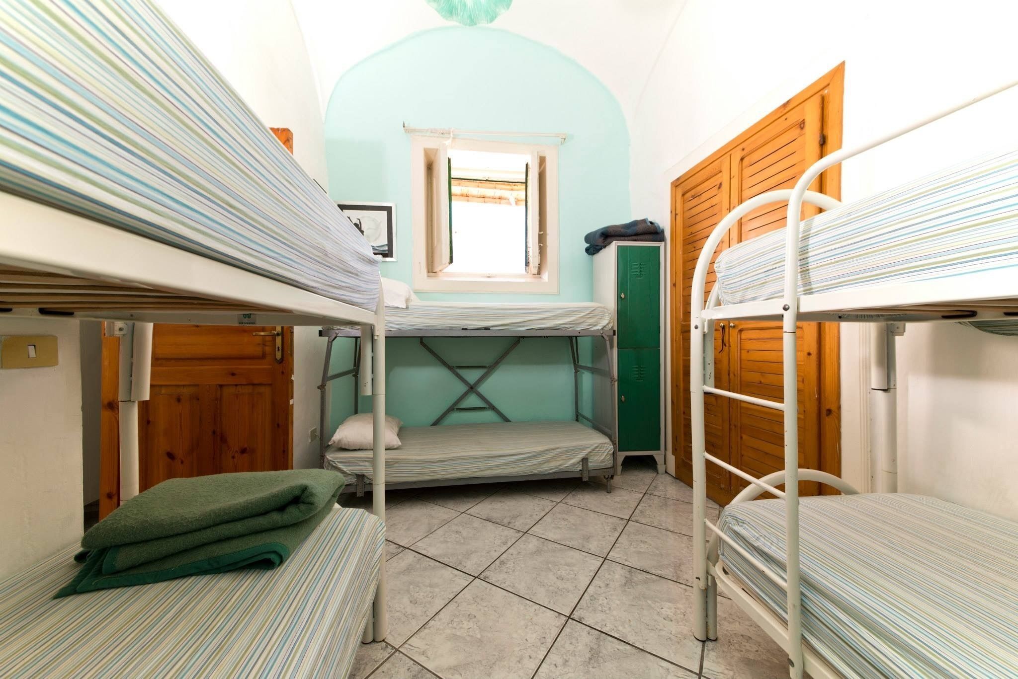 A dormitory room with bunk beds, a window, and a door.