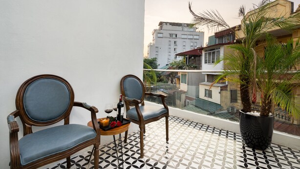 A balcony with two wooden chairs, a small table with a bottle and flowers, and a potted plant. - Memory Legends Hotel (Hanoi)