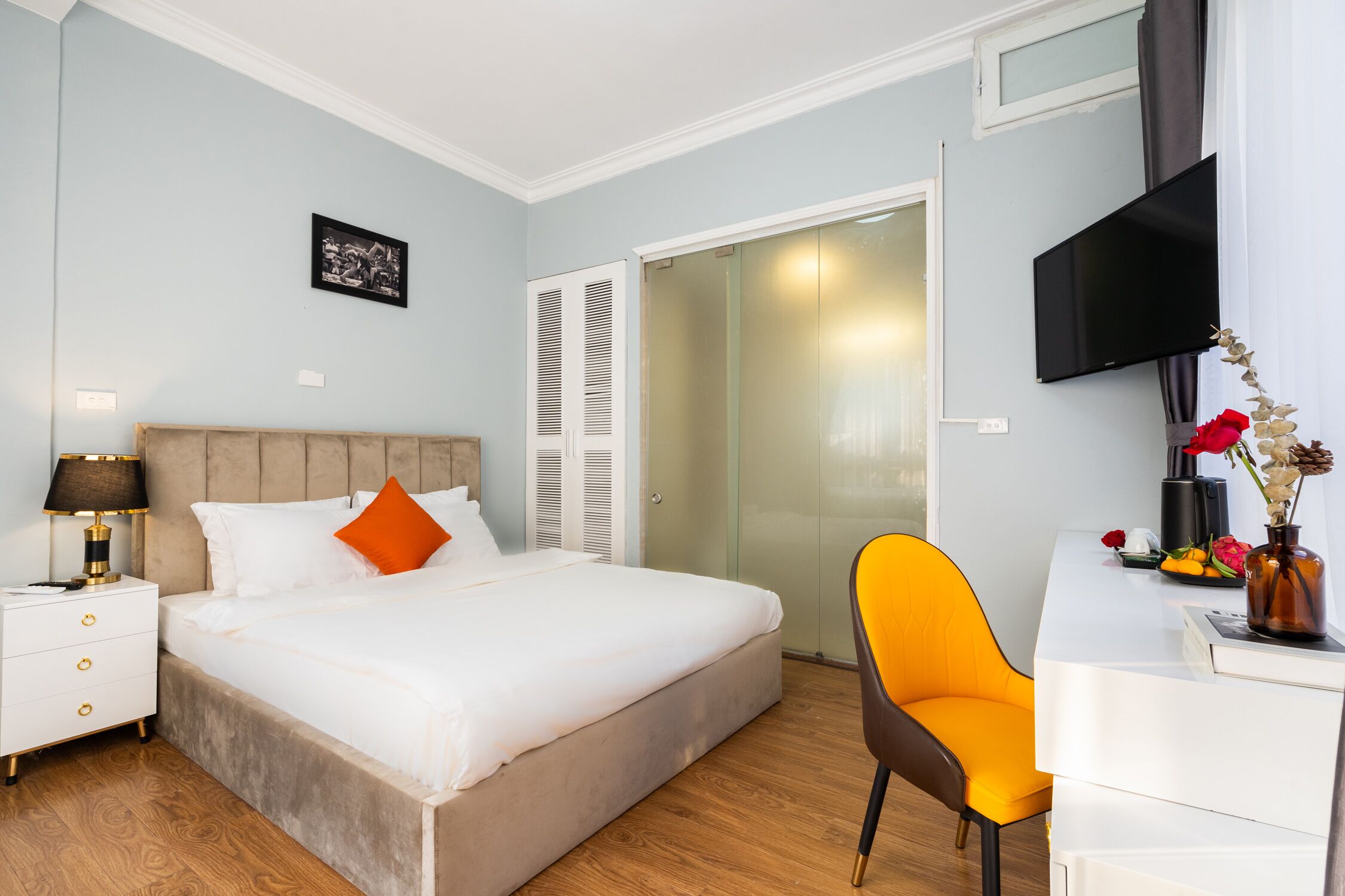 A bedroom with a bed, nightstand, desk, chair, and a TV.