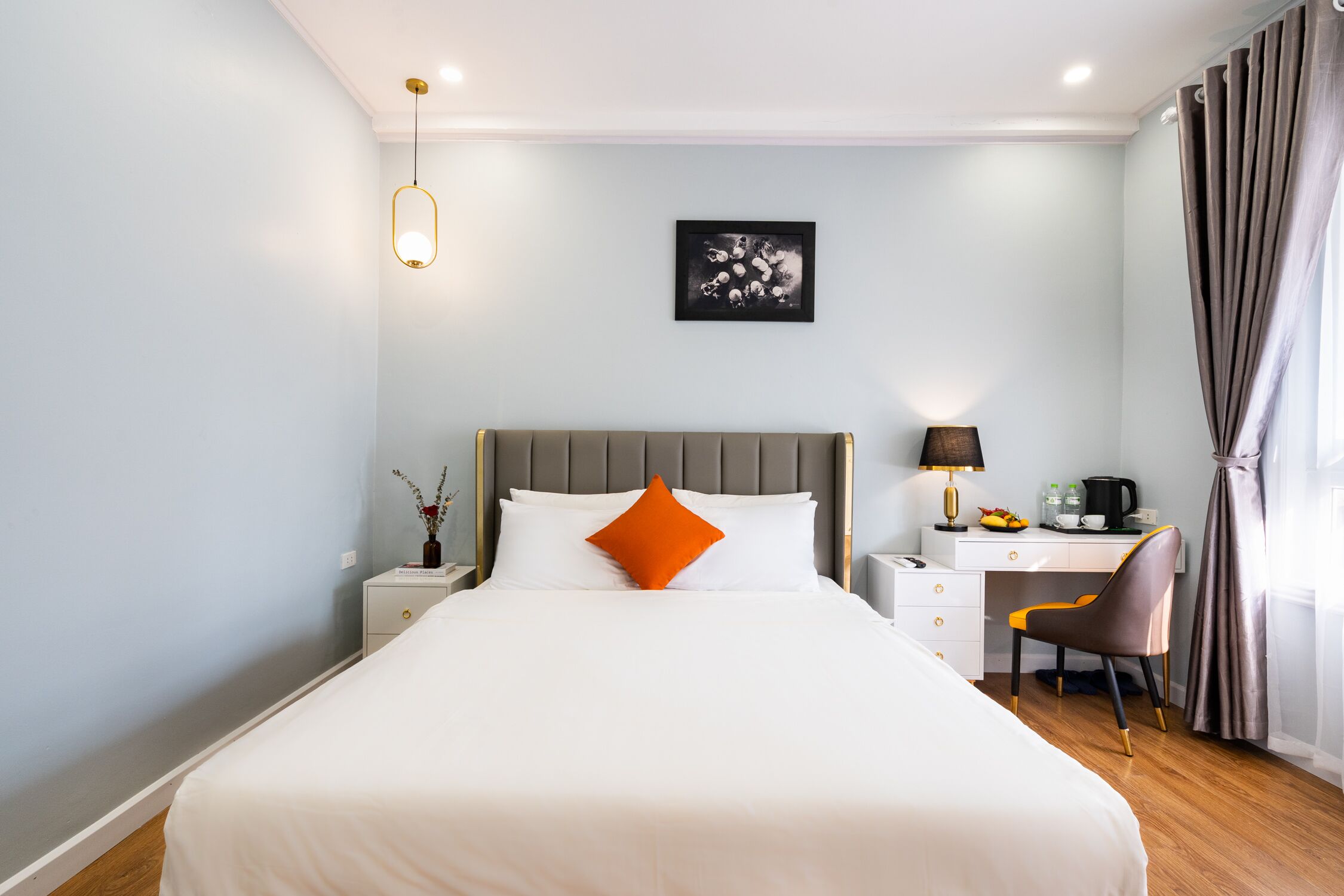 A hotel room with a bed, a desk, a chair, a nightstand, a lamp, and a picture on the wall.