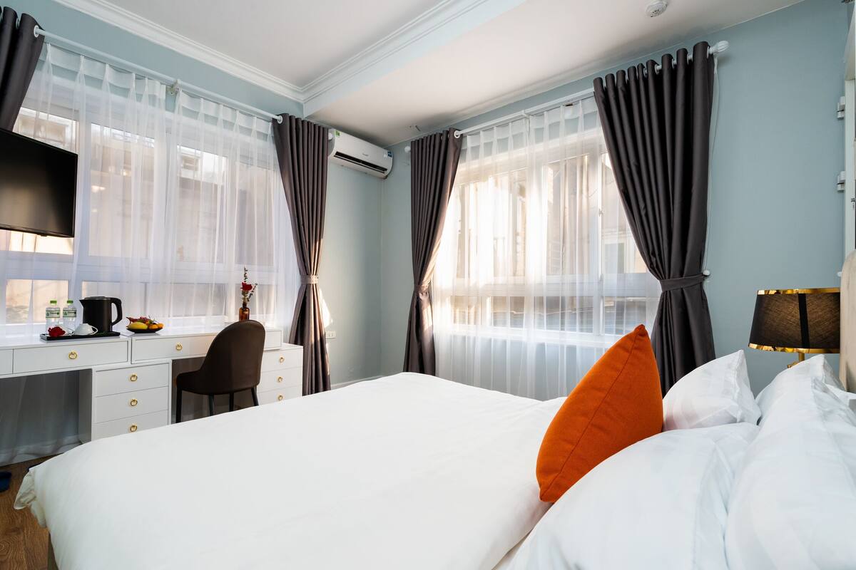 A hotel room with a bed, a desk, a chair, and a window with curtains.
