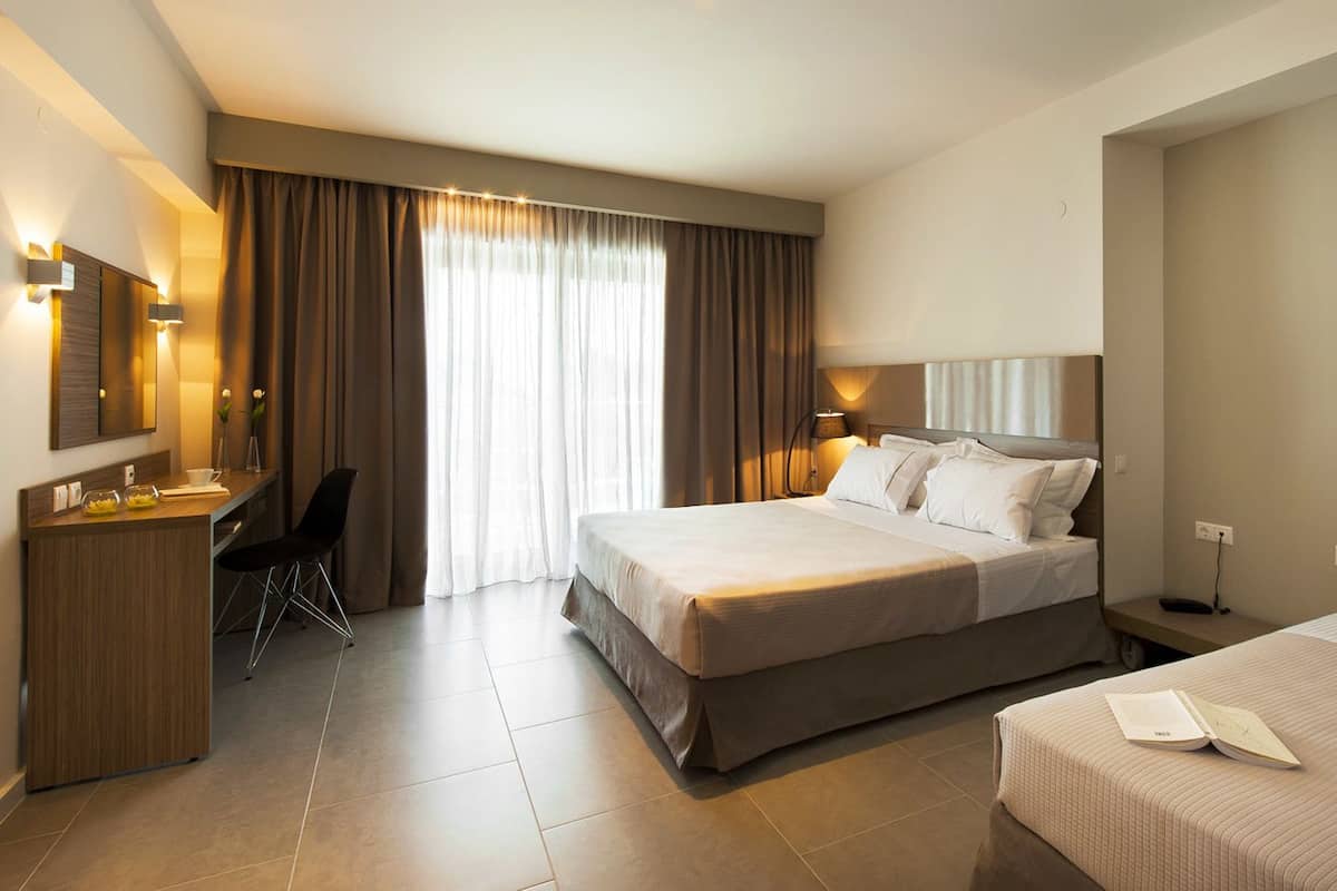 A hotel room with a large bed, a desk with a chair, a bedside table, and a mirror.