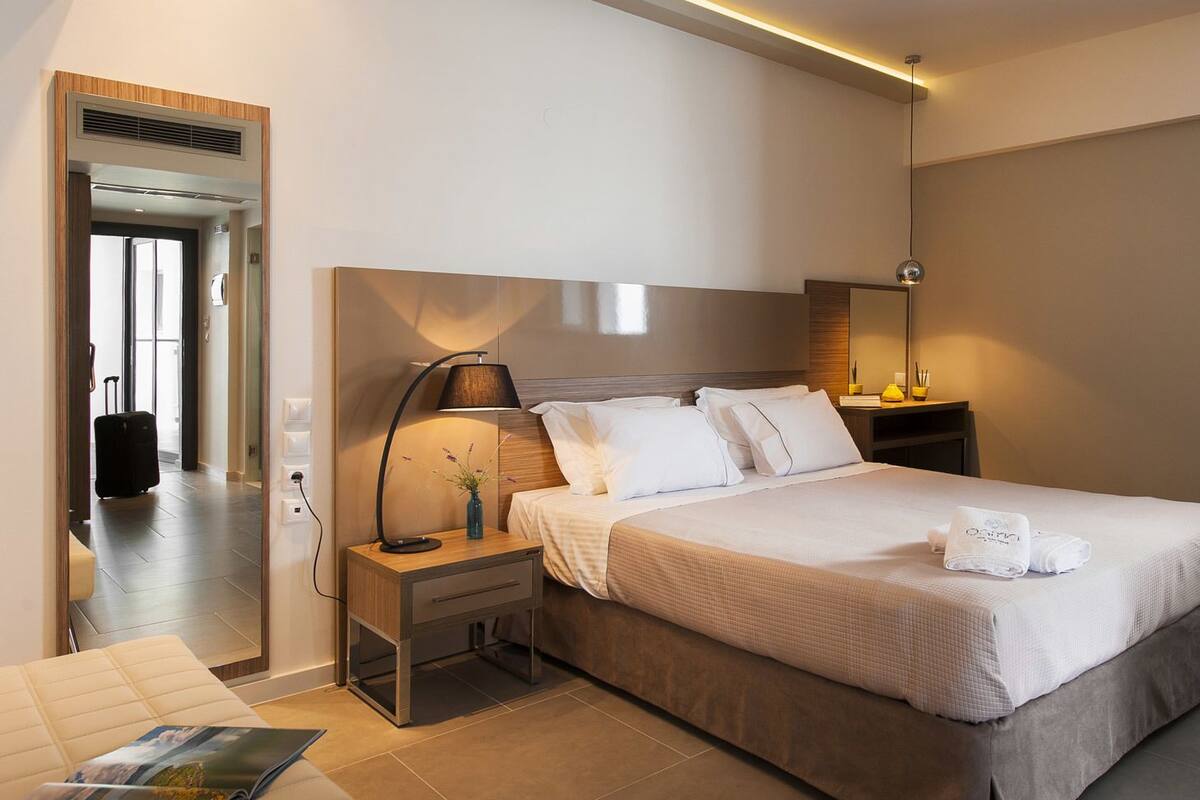 A modern hotel room with a large bed, bedside tables, a lamp, and a view of the hallway.