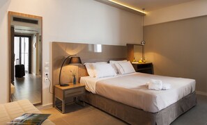 Ein modernes Hotelzimmer mit einem großen Bett, Nachttischen, einer Lampe und Blick auf den Flur.