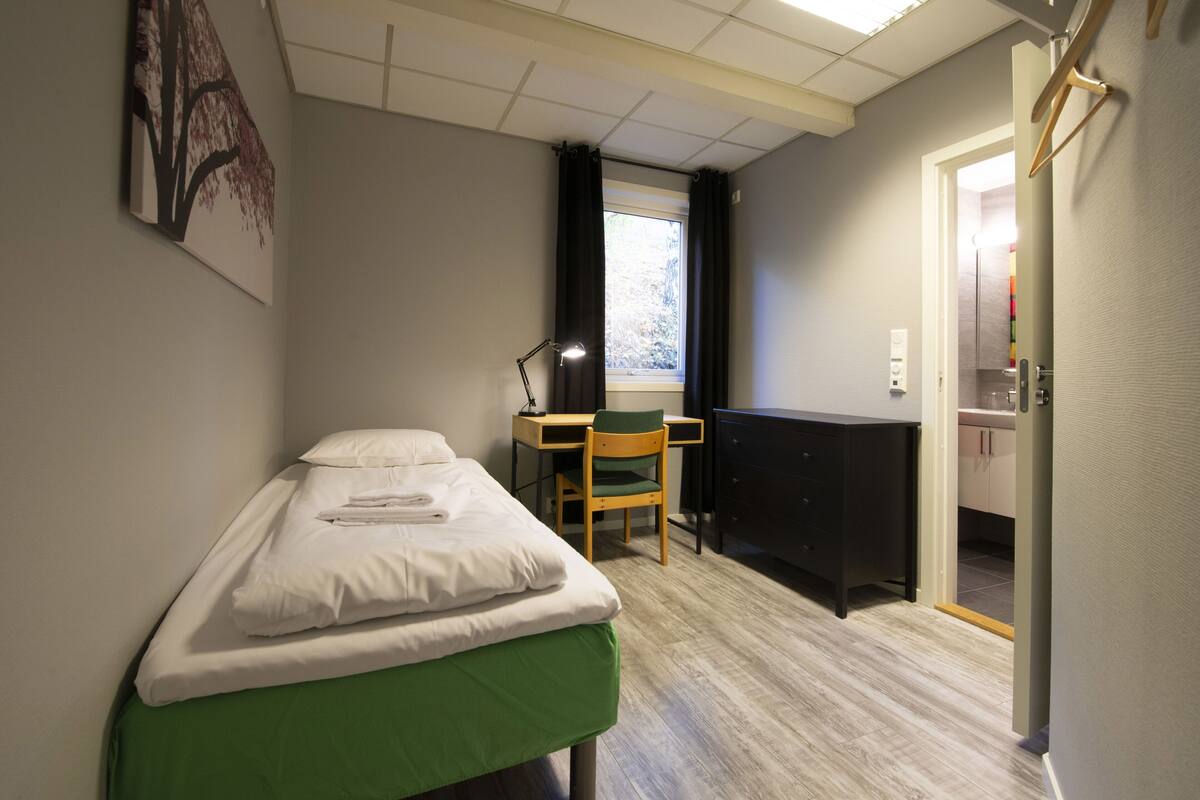 Ein kleines Zimmer mit einem Bett, einem Schreibtisch und einem Stuhl.