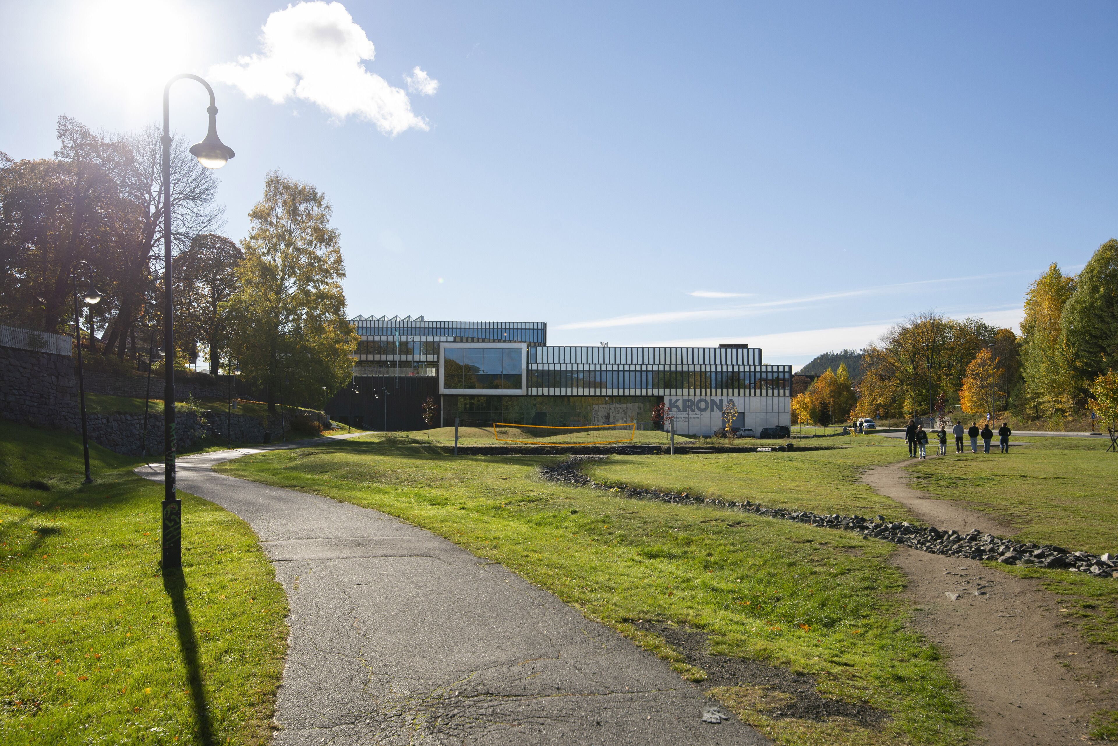 A pathway leading to a modern building with a glass facade, surrounded by grass and trees.
