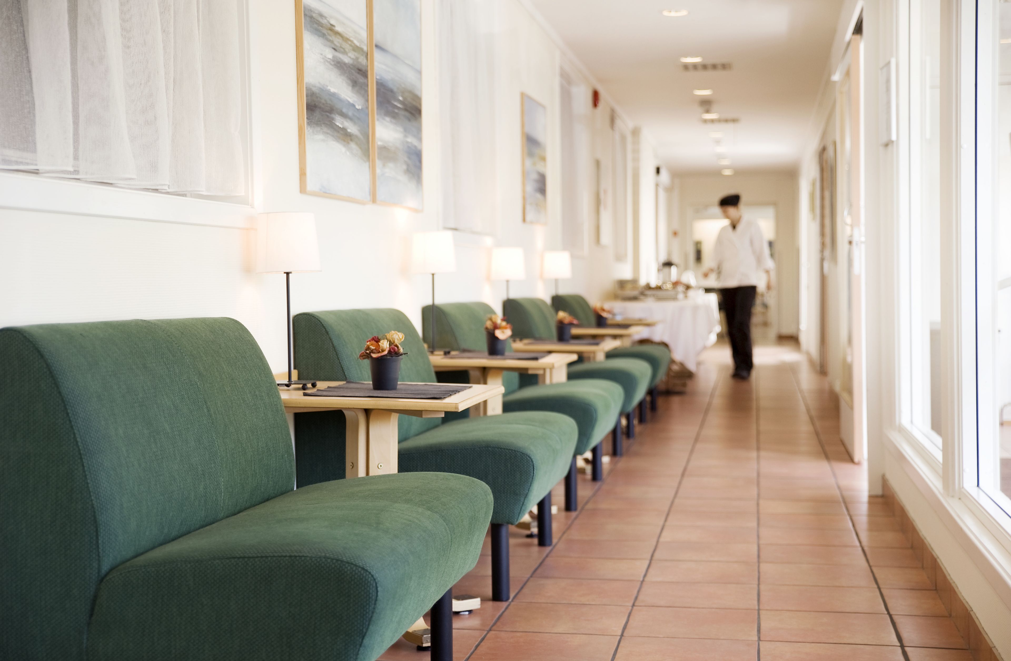 Passadís d'hotel amb seients tapissats de verd, taules amb làmpades i obra d'art a les parets.