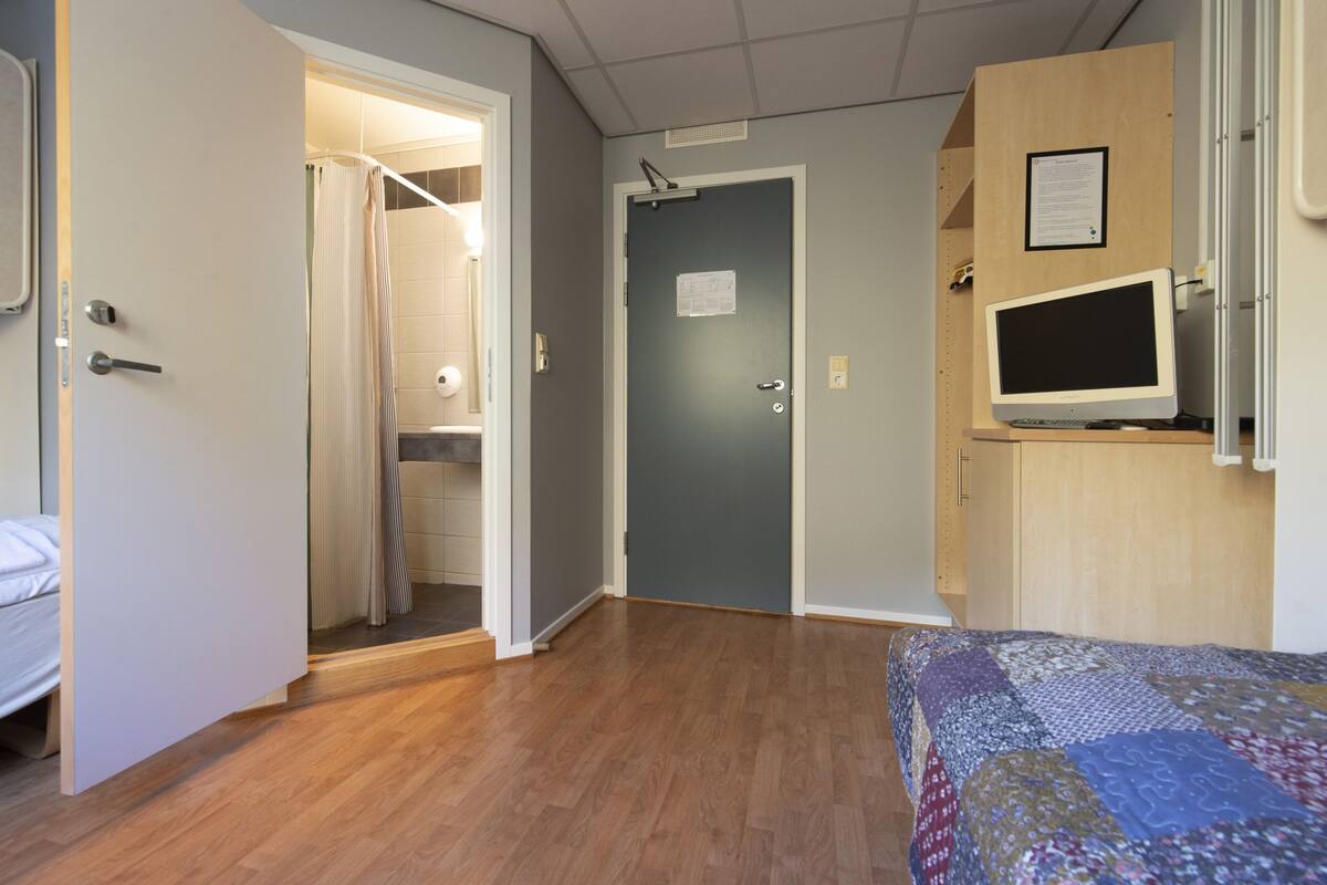 Ein Zimmer mit einem Bett, einem Schreibtisch mit Computer und einer Tür zu einem Badezimmer.