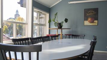 Een vergaderruimte met een grote tafel en stoelen, een projector die aan het plafond is bevestigd, en een raam met uitzicht op gebouwen en bomen.