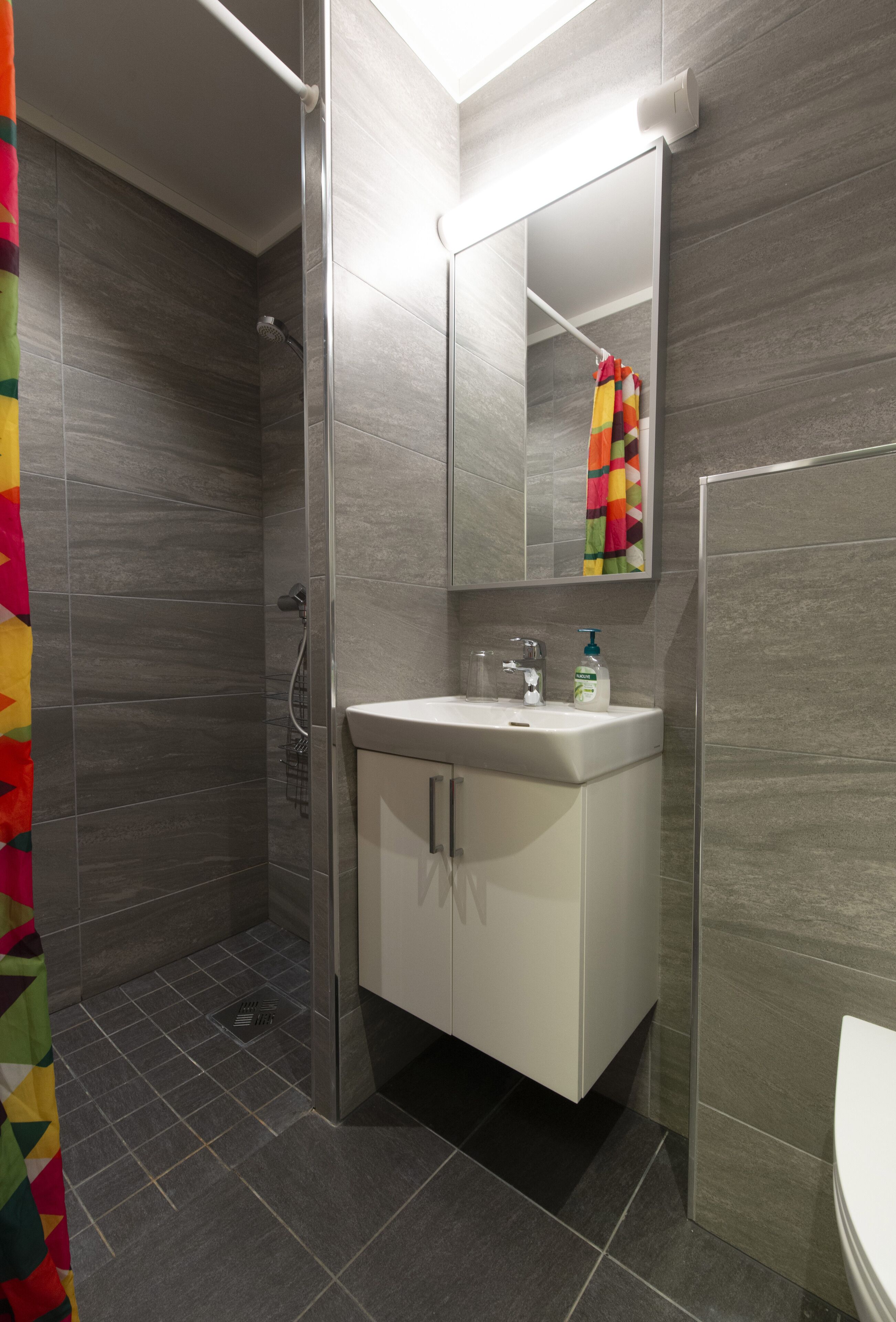 Un baño moderno con ducha, un lavamanos con espejo y una toalla colgada en la pared.