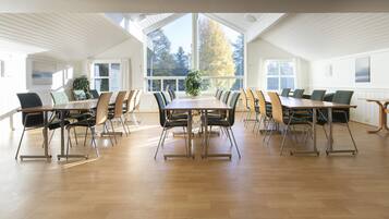 A conference room with a long table and multiple chairs, large windows with curtains, and a wooden floor.