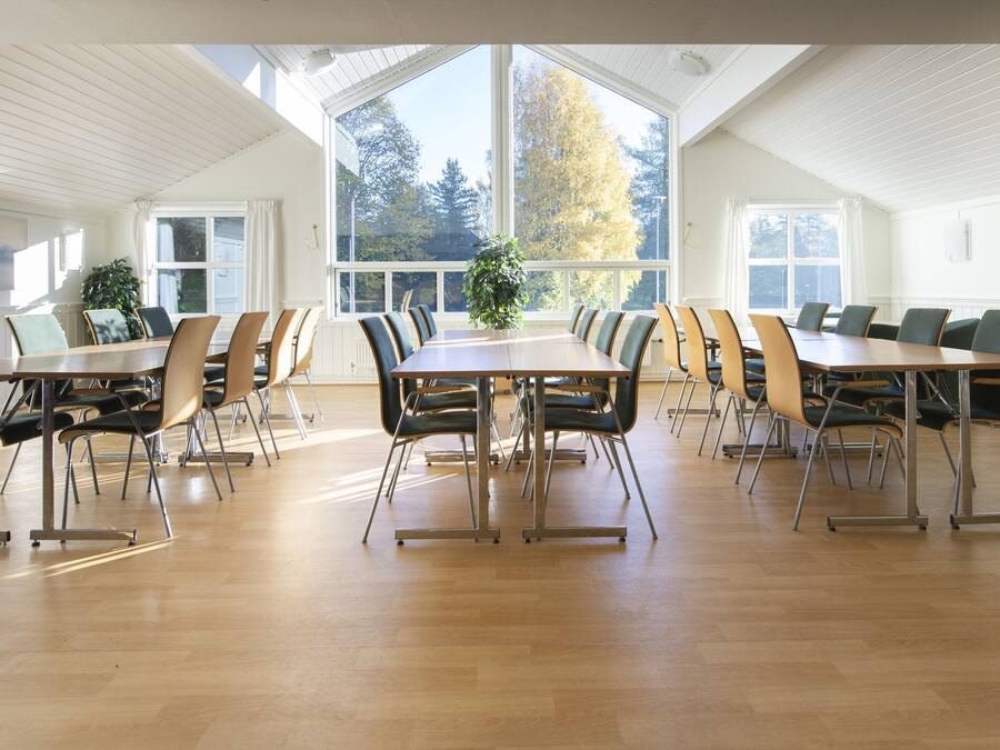 A conference room with a long table and multiple chairs, large windows with curtains, and a wooden floor.