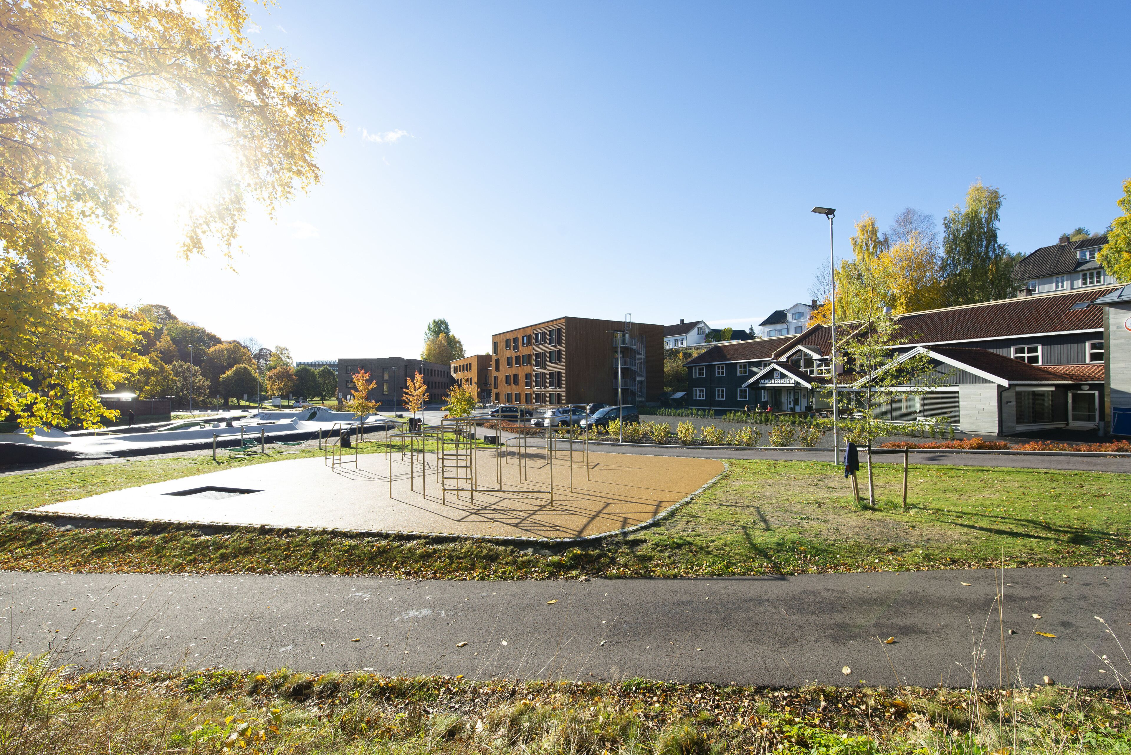A park with a playground, a parking lot, and residential buildings in the background.