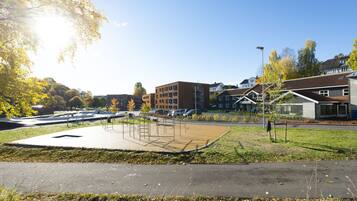 A park with a playground, a parking lot, and residential buildings in the background.