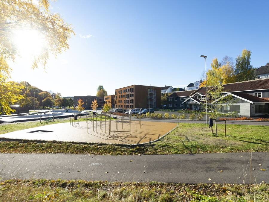 A park with a playground, a parking lot, and residential buildings in the background.