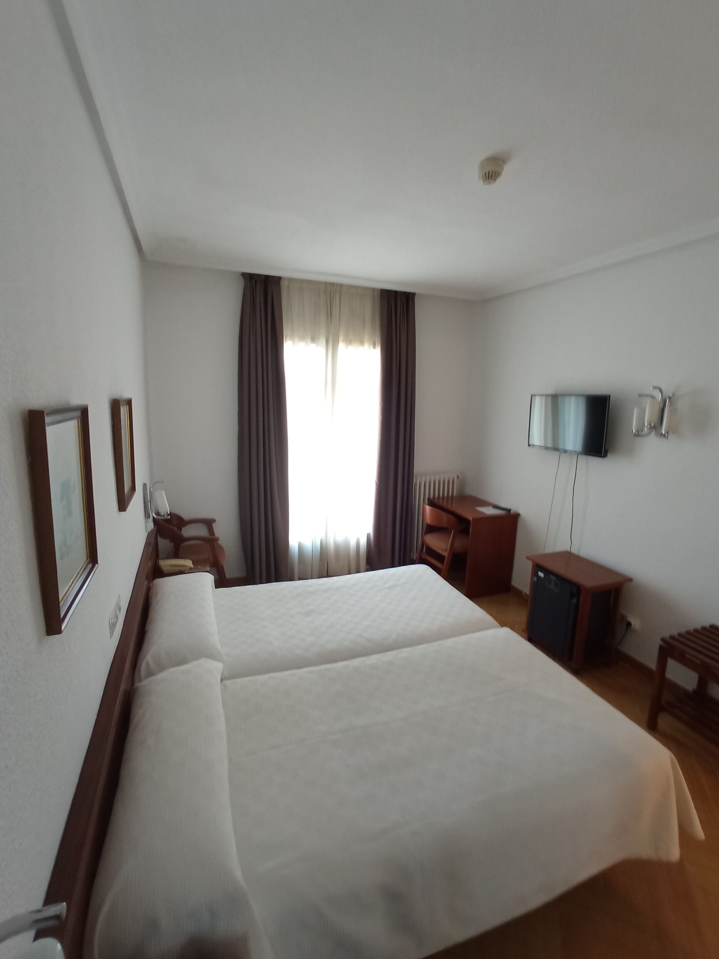 A hotel room with two beds, a desk, a chair, a TV, and a small cabinet.