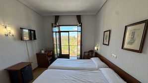 Et hotelværelse med to senge, et skrivebord, en stol, et fjernsyn og en balkon med udsigt.