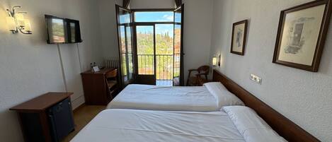 A hotel room with two beds, a desk, a chair, a TV, and a balcony with a view.