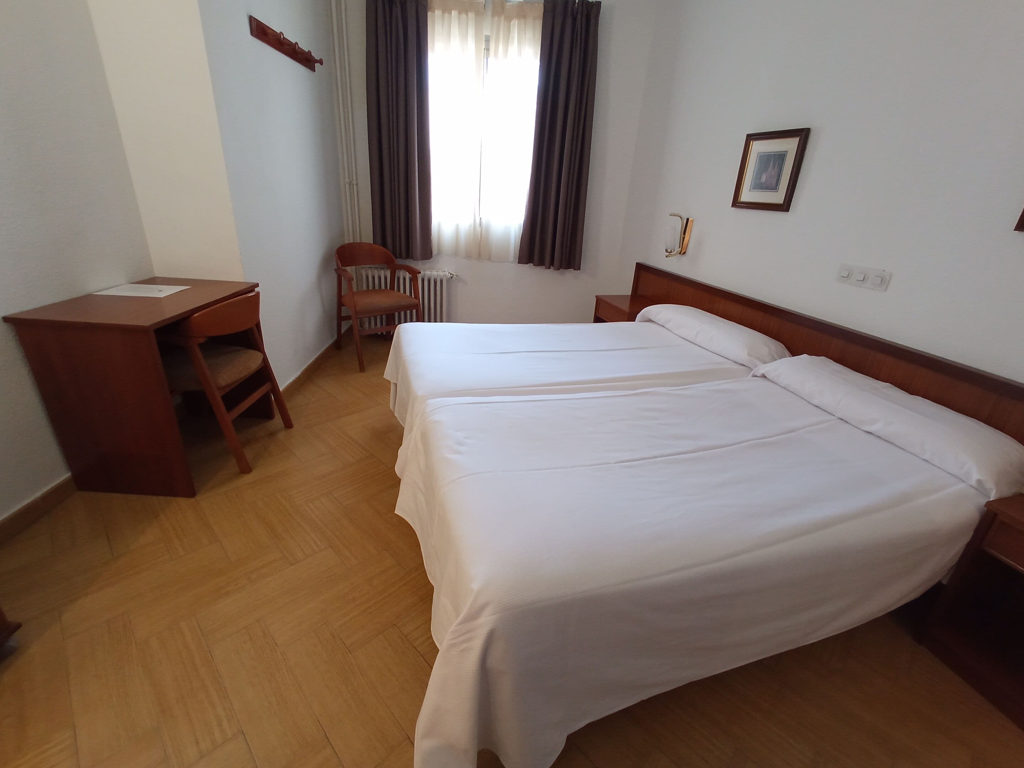Ett hotellrum med två sängar, ett skrivbord, en stol och ett element.