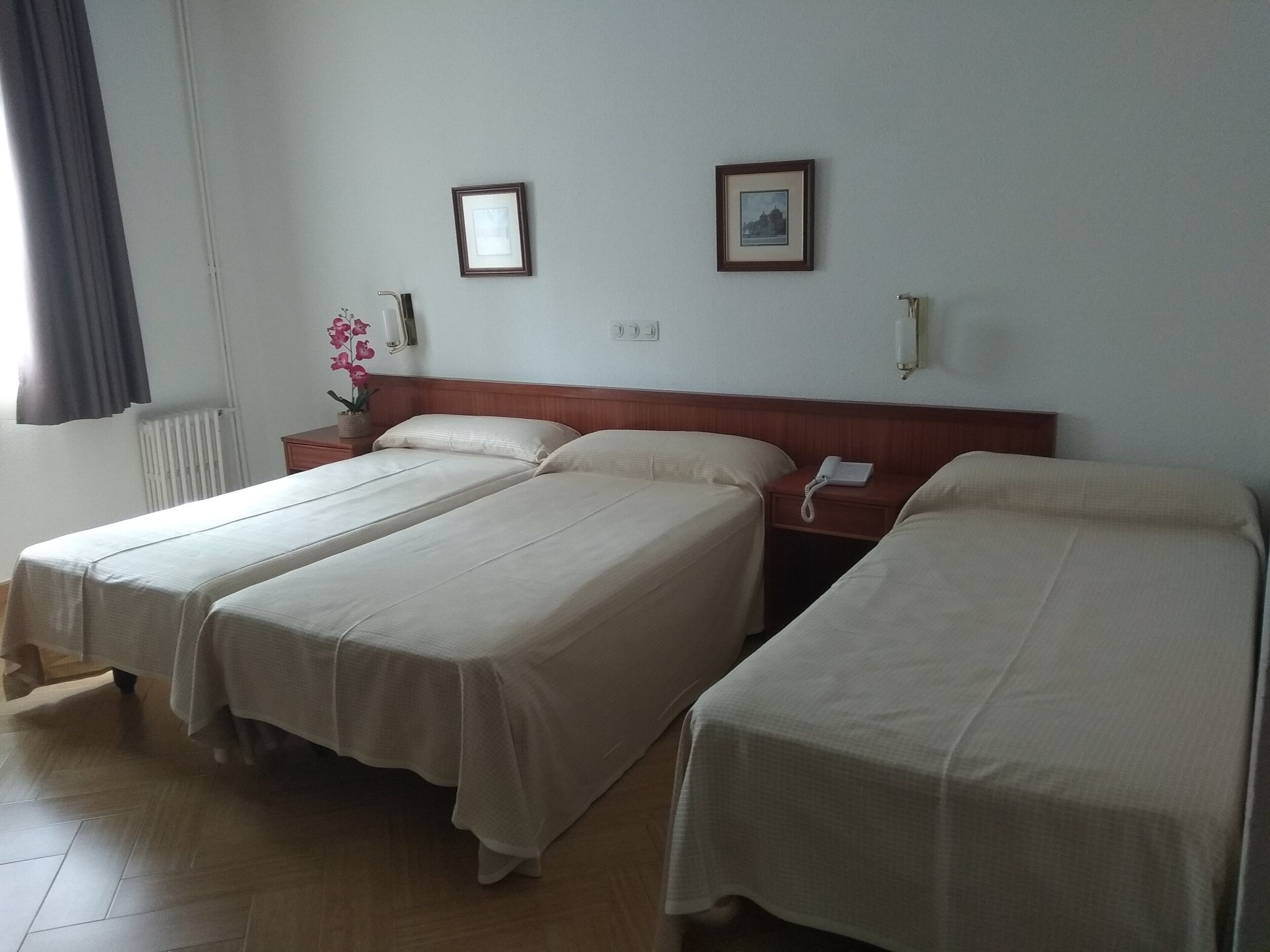 Habitación de hotel con dos camas individuales, cabecera de madera, mesita de noche con teléfono y radiador.