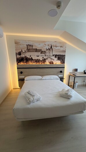 Habitación de hotel con una cama grande, cabecera de madera, un escritorio con silla y una lámpara de pared.