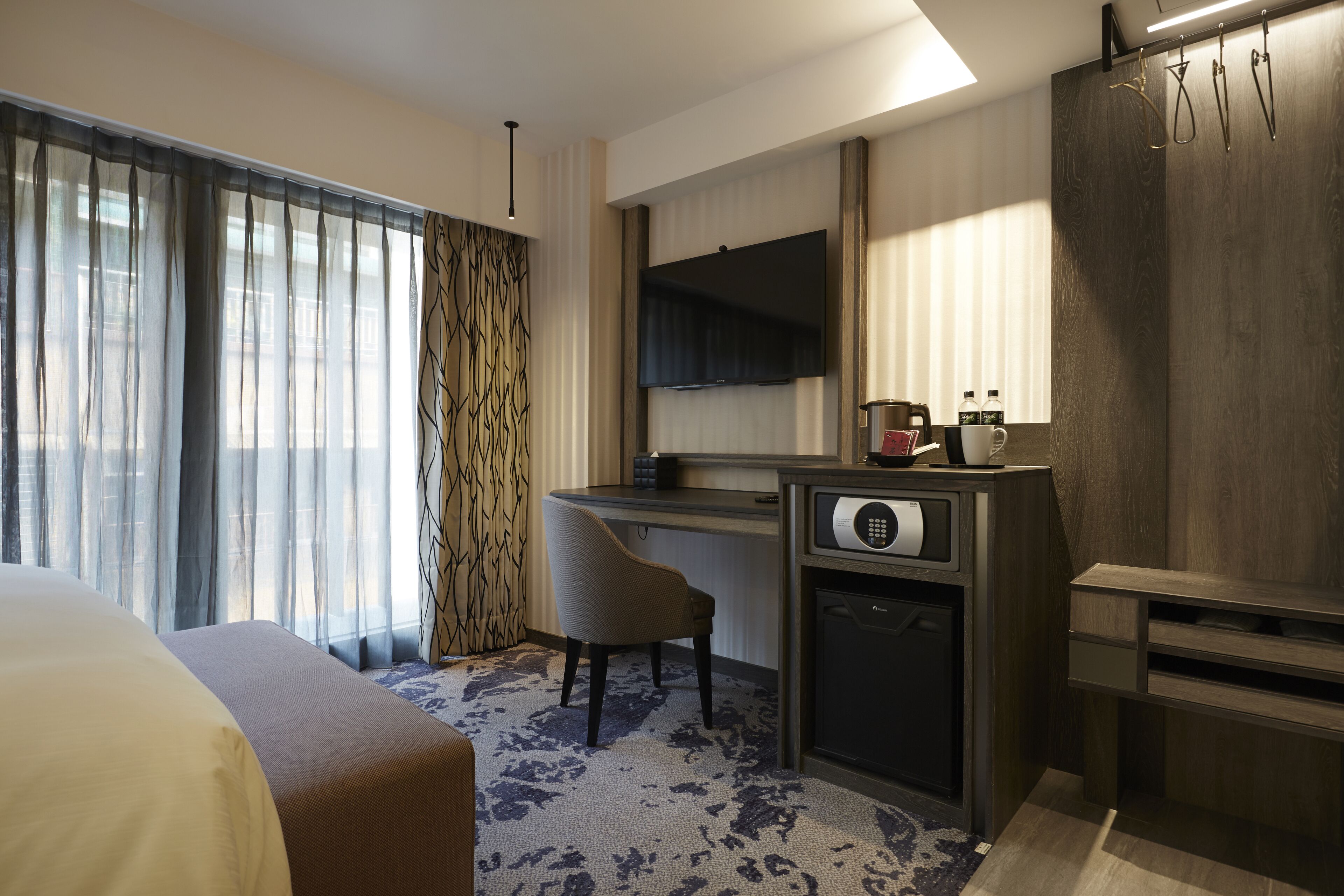 A hotel room with a bed, a desk, a chair, a television, and a minibar.