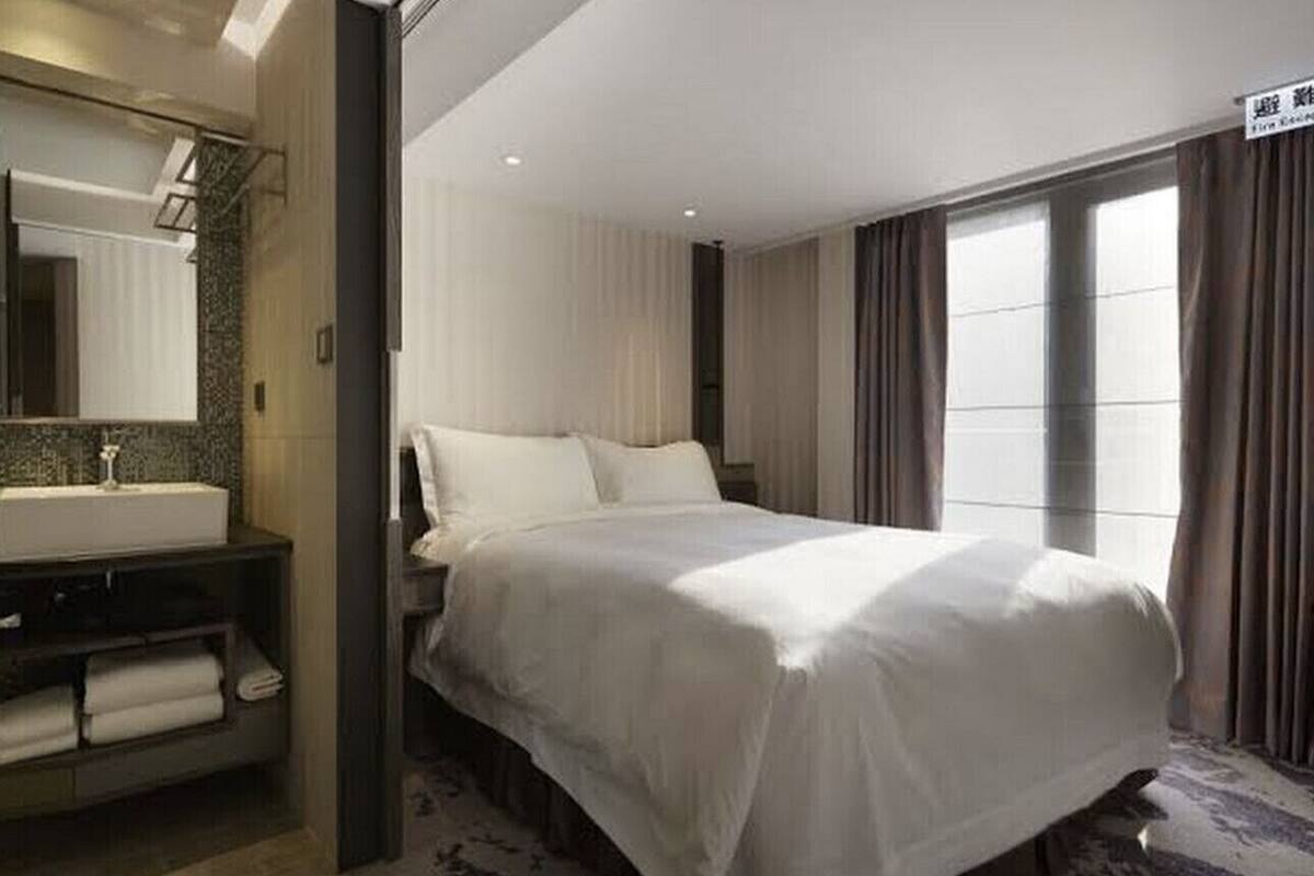 A hotel room with a large bed, a bathroom with a sink and towel rack, and a window with curtains.