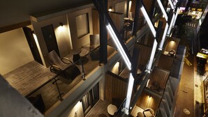 A multi-level hotel interior with a modern design, featuring a staircase connecting different floors, seating areas with tables and chairs, and a view of the street outside. - At Home Hotel Ximen (Taipei)