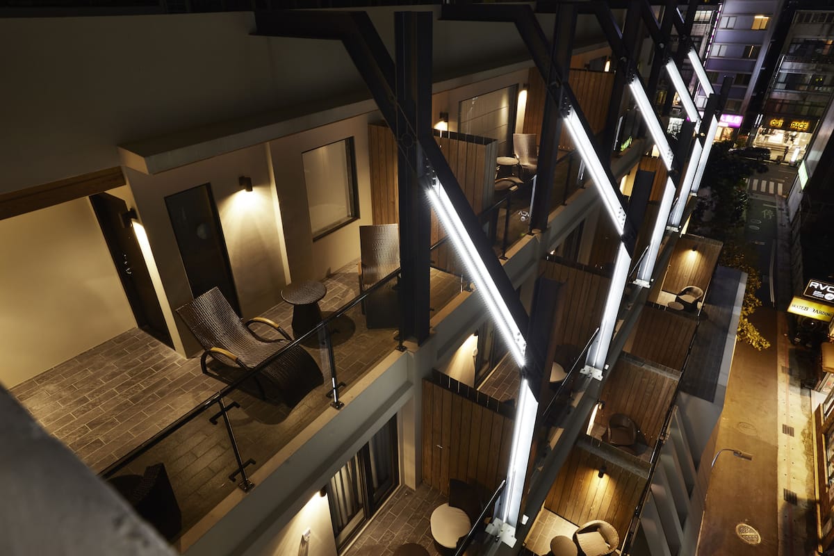A multi-level hotel interior with a modern design, featuring a staircase connecting different floors, seating areas with tables and chairs, and a view of the street outside.