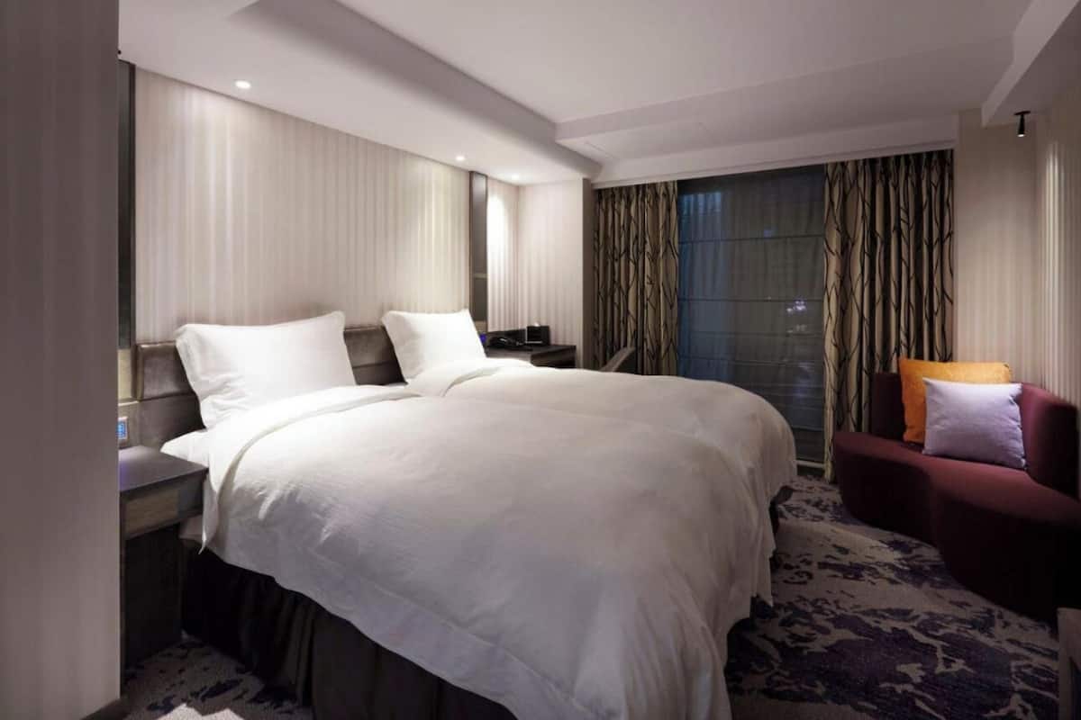 A hotel room with a large bed, a desk, a chair, and a window with curtains.
